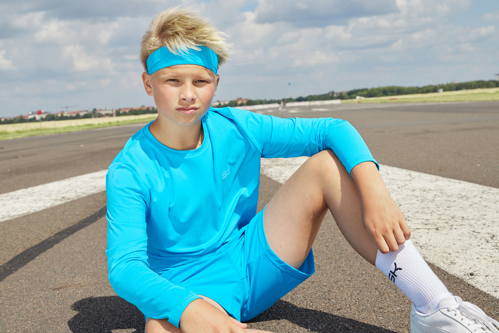Junge mit hellblauem Longsleeve Shirt, Shorts und weißen Sportsocken von Sportkind