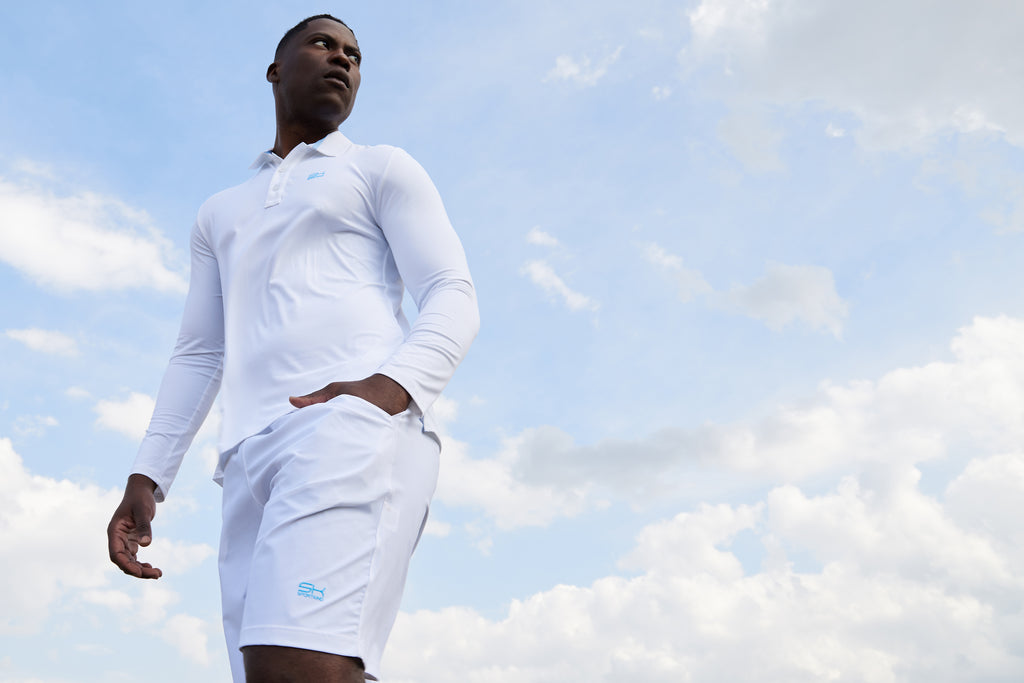 Mann mit weißer Sportkleidung von Sportking, bestehend aus Lonsleeve Polo Shirt und Shorts