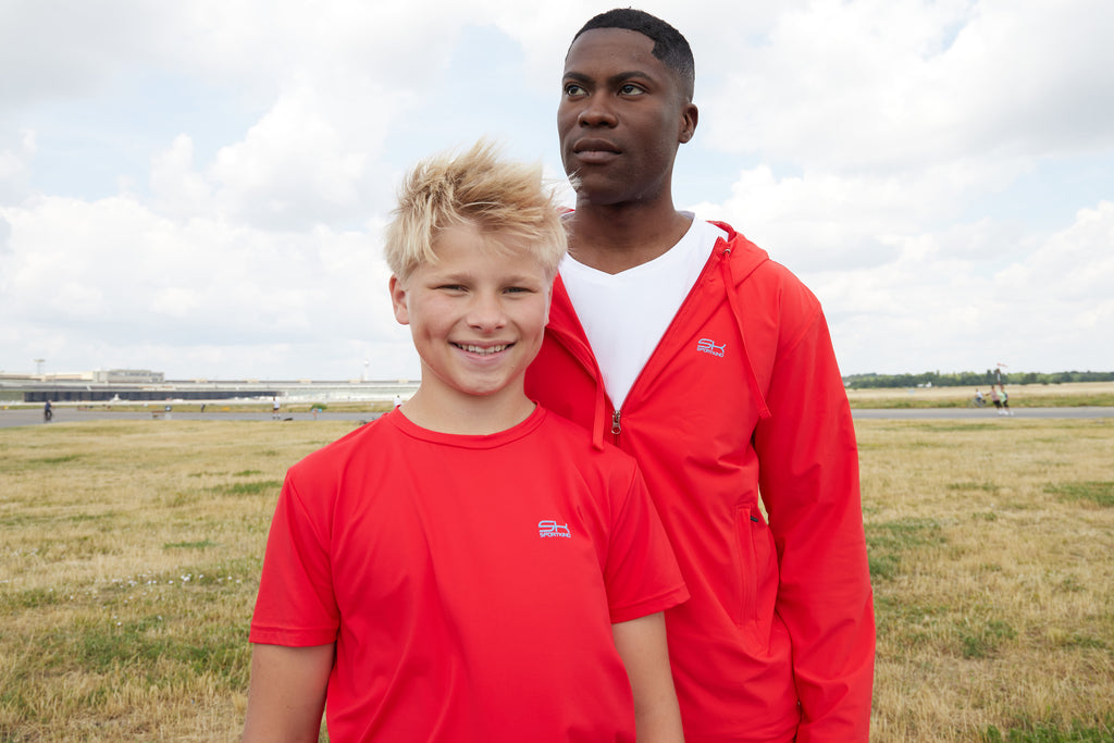Junge mit rotem T-Shirt und Mann mit weißem V-Neck T-Shirt und roter Sportjacke von Sportkind