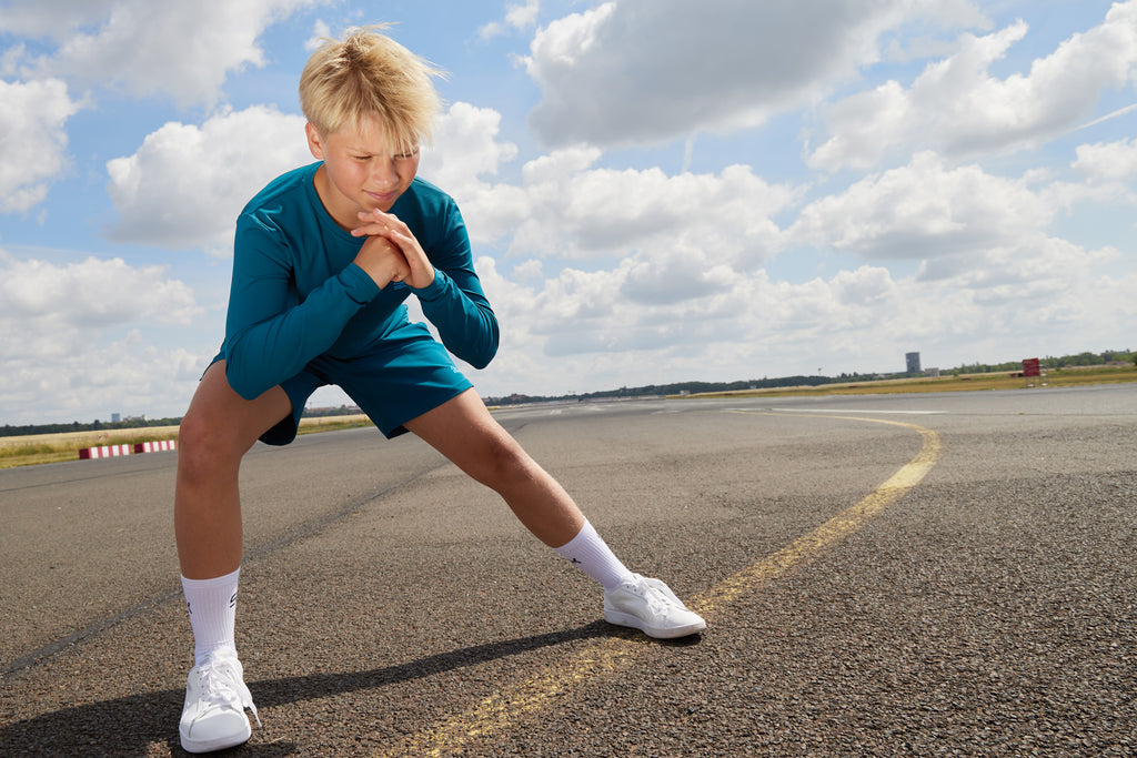 Junge mit petrolfarbener Sportkleidung bestehend aus Longsleeve und Shorts kombiniert mit weißen Sportsocken von Sportkind