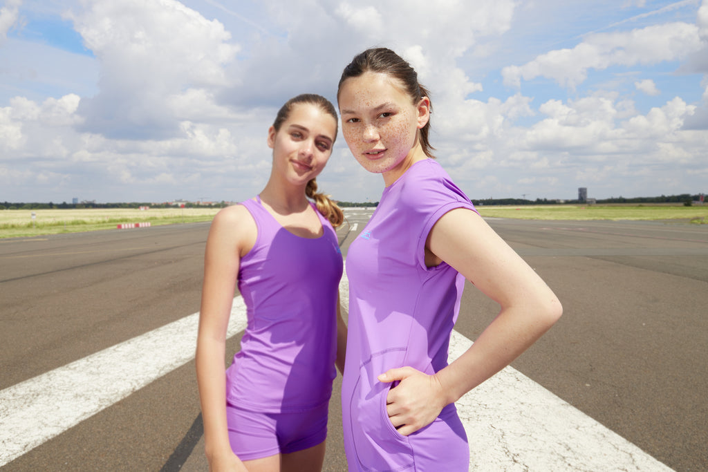 Mädchen mit lilafarbenem Loosefit Kleid und Mädchen mit lilafarbenem Top und Shorts von Sportkind